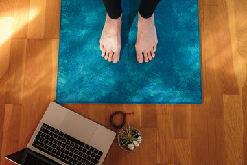 Woman feet over a mat prepared for the morning yoga practice online in front of a laptop. Yoga at home, top view.