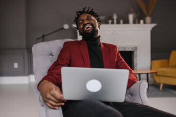 Smiling handsome young african american guy sitting, looking at computer screen. Focused millennial biracial man working on project in modern office or studying online at home.