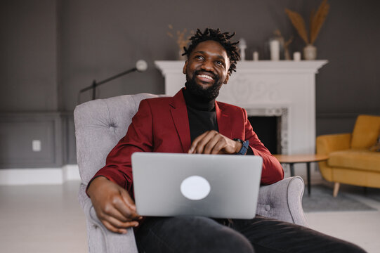 Smiling handsome young african american guy sitting, looking at computer screen. Focused millennial biracial man working on project in modern office or studying online at home.