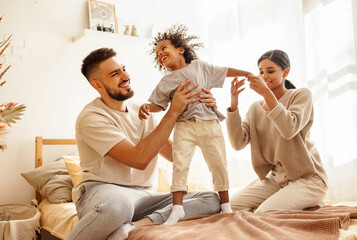 happy diverse family mom, dad and child  laughing, playing and jumping   in bed   at home.