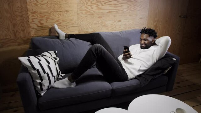  black man resting on the couch and looking at the phone