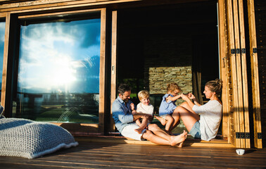 Family with small children sitting on patio of wooden cabin, holiday in nature concept.