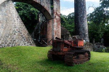 Fototapeta na wymiar An old tractor lies in front of the ruins of the abandoned Wingfield Estate Sugar Plantation in St. Kitts in the Caribbean.