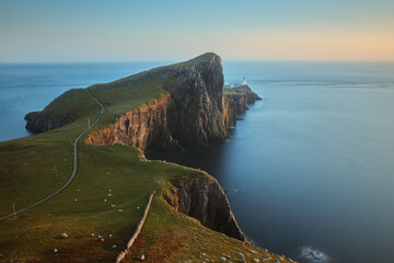 Fototapeta na wymiar A scenery of a fine lighthouse standing on a stunning cliff against the backdrop of the sea and lit by the setting sun. Neist Point, Isle of Skye, Scotland
