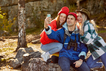 three caucasian friends enjoy spending time in the forest after climbing mountains, take photo on smartphone. travel and adventure, trip concept. active youth relax, lead sportive healthy lifestyle