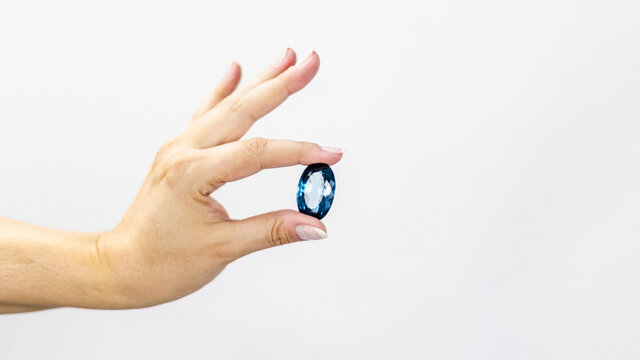 Elegant woman's hand holds a large deep blue topaz stone on isolated white background