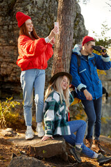 young caucasian friends in sportive bright wear enjoy time on mountains together, relax after climbing, happy travellers in nature