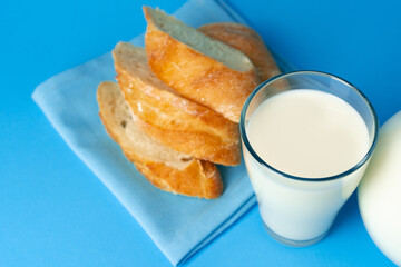 Fresh baguette bread and pitcher with fresh milk on blue background