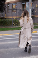 Fototapeta premium beautiful slim young brunette in fashionable trench coat and black dress cross a pedestrian crossing.