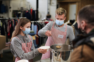 Volunteers serving hot soup for homeless in community charity donation center, coronavirus concept.