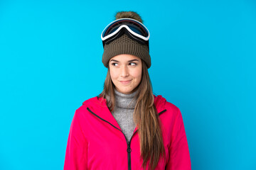 Teenager skier girl with snowboarding glasses over isolated blue background standing and looking to the side
