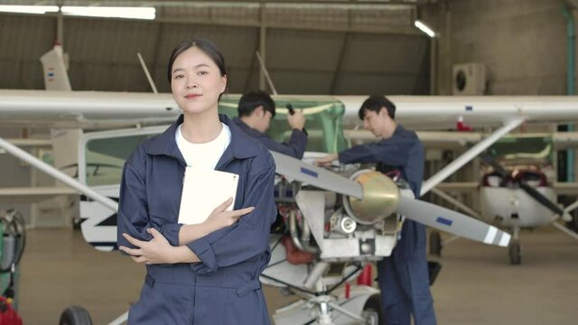 Portrait of young asian aircraft maintenance engineer standing in airplane hangar looking at camera with arms crossed. 