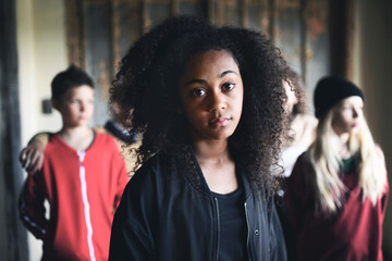 Portrait of mixed-race teenager girl with friends standing indoors in abandoned building. - obrazy, fototapety, plakaty