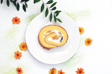 ロールケーキとテーブルに散りばめたオレンジ色の花