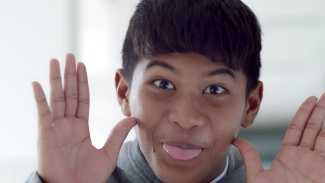 A smiling Asian boy, bang hair and tan skin is greeting by stick out funny tongue.