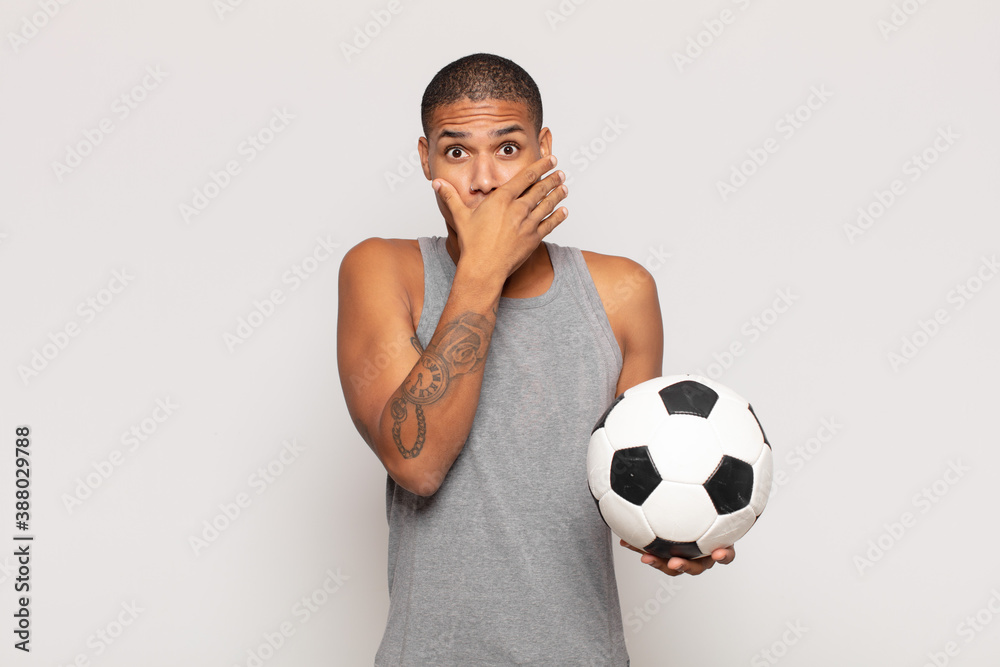 Wall mural young black man covering mouth with hands with a shocked, surprised expression, keeping a secret or saying oops