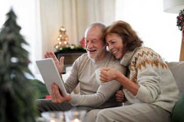 Side view of senior couple indoors at home at Christmas, having video call with family.