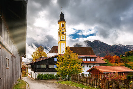 The mountain town Pfronten with dramatic sky and amazing sun lighting on a golden autumn day. Saint Nicholas church and old wooden houses in Pfronten, Alps, Allgau, Bavaria, Germany