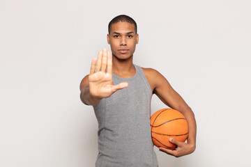 young black man looking serious, stern, displeased and angry showing open palm making stop gesture