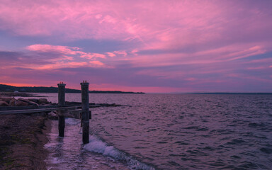 Sunset seascape at the beach with ruined pilings and pink clouds above