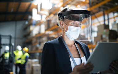 Manager with protective shield uisng tablet indoors in warehouse, coronavirus concept.