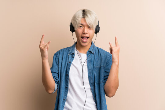 Young Asian Man Over Isolated Background Using The Mobile With Headphones And Dancing