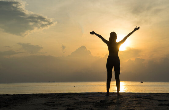 Silhouette of Asian girls stand with arms raised to feel free  and enjoying  life on the beach at sunrise  in morning .Freedom  and Wellbeing concept.