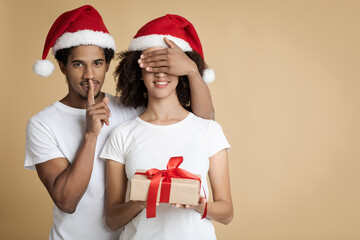 African american man in hat shows sign of silence, closes eyes to his wife and gives her box
