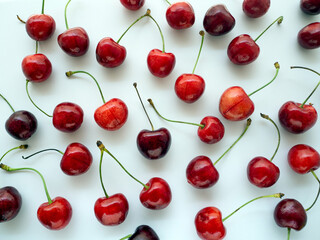Obraz na płótnie Canvas Ripe red cherry with twigs evenly distributed over a white background. Food background with berries.