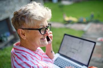 Senior woman architect with smartphone working outdoors in garden, home office concept.