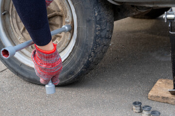 A woman with a wheel wrench unscrews a wheel from a car to replace it.