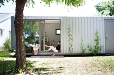 Mature woman working in home office in container house in backyard, resting.