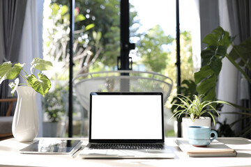 Laptop white mock up screen with blue cup and plant pot and notebook and tablet interior work from...