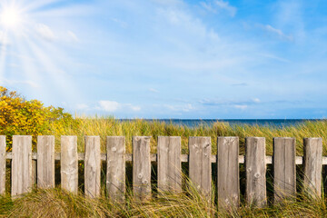 wooden fence on beach grass covered dunes against sea and blue sky