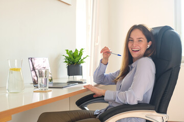 Young business woman is doing an online call with her colleagues through digital technology. She is smiling and sitting at her home office and keeping social distanc. Beautiful light modern interior.