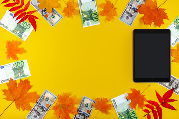 Tablet computer with autumn leaves and dollar and euro banknotes.