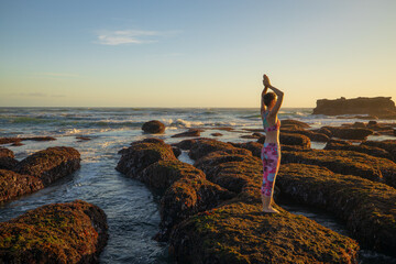 Caucasian woman standing on big stone during low tide. Yoga and meditation at the beach. Hands...
