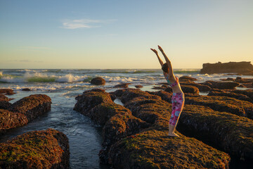 Hasta Uttanasana. Deflection back. Caucasian woman standing on big stone. Low tide. Yoga practice...