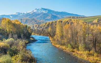 Fototapeta na wymiar River, forested banks and a snow-capped peak. Sunny autumn day.
