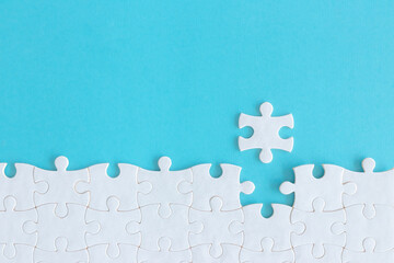 Assembling jigsaw puzzle pieces, Top view unfinished white jigsaw puzzle on blue background, Fragment of a folded white jigsaw puzzle with copy space, Teamwork and problem solving concept. - obrazy, fototapety, plakaty