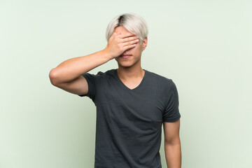 Young asian man over isolated green background covering eyes by hands. Do not want to see something