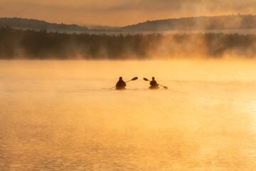 Obraz na płótnie Canvas Kayakers paddling in lake of two rivers Algonquin Park with early morning fog and sun light