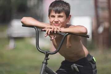 A child with an old Bicycle on the street. A white boy sits on an outdated Bicycle on a summer day.
