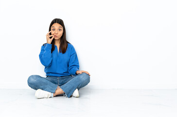 Young mixed race woman sitting on the floor isolated on white background showing a sign of silence...