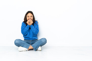 Young mixed race woman sitting on the floor isolated on white background happy and smiling covering mouth with hands