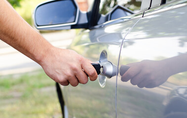 Male hand inserting a key into the door lock of a car