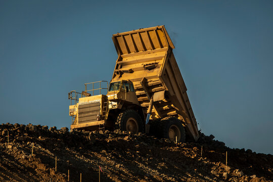 A Very Large Yellow Haul Dump Truck On A Ridge At A Construction Site Involved In Grading Operations. The Bed At The Back Of The Truck Is Lifted Up