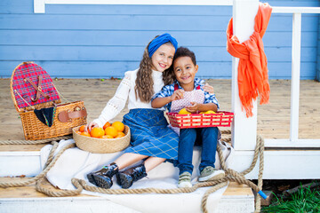 Happy boy and girl are sitting on the porch of the house with fruits