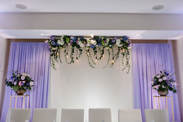 Festive table, arch, stands decorated with composition of violet, purple, pink flowers and greenery in the banquet hall. Table newlyweds in the banquet area on wedding party.