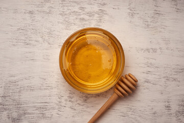 Fresh acacia honey in a glass bowl near a wooden honey spoon, top view